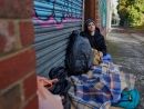 Image of an individual experiencing homelessness shelters in an alleyway garage doorway.