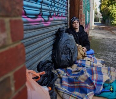 Image of an individual experiencing homelessness shelters in an alleyway garage doorway.