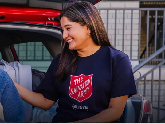 Female Salvos Officer supporting a young woman sitting in the boot of her car.