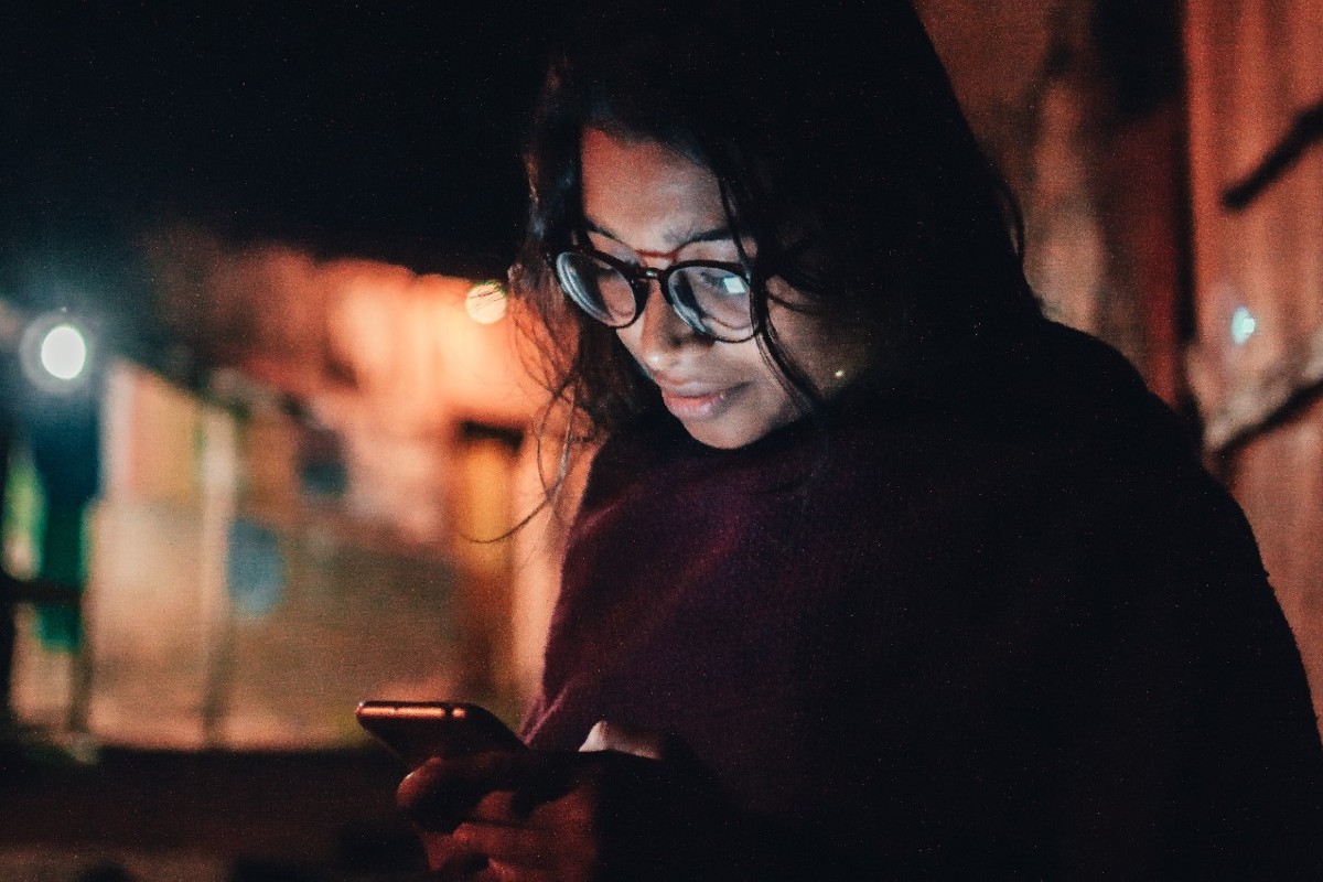 A phone screen lights up a woman's face in the darkness.