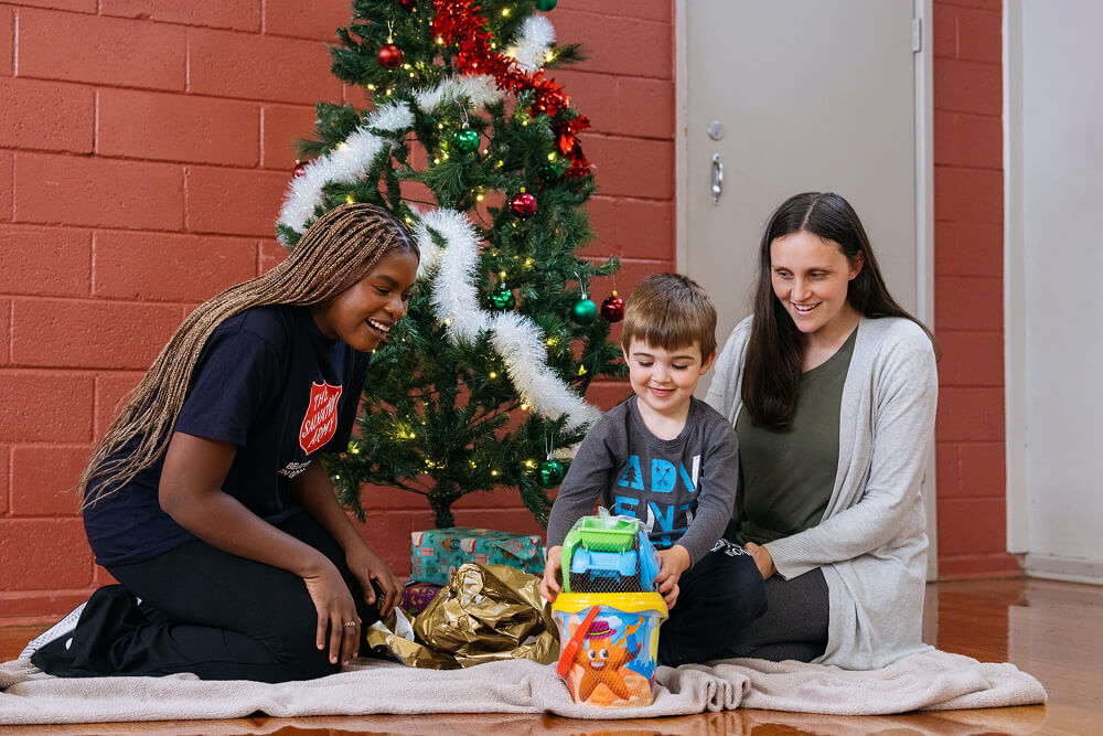 Salvos personnel and mother smiling watching a son play with his Christmas gift