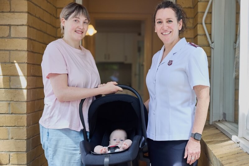 Emily with her daughter in a pram smiling and standing next to a Salvos personnel