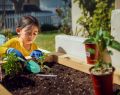 A young girl planting various plants using a shovel in a sunny garden.