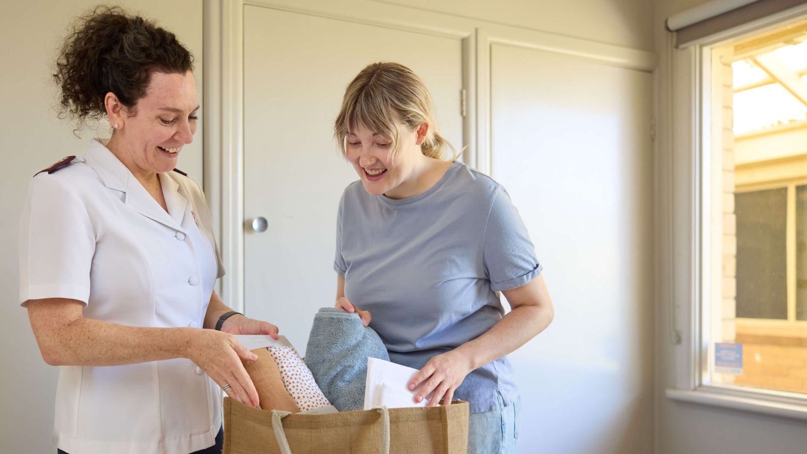 Salvos personnel handing a hamper filled with groceries to a mother in need