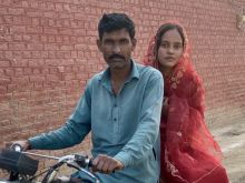 Nisha on the back of a motorcycle. A man is in front of her on the bike holding onto the handles.