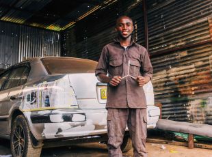 A man holds up an enormous bunch of slightly green bananas he has harvested from his plantation.
