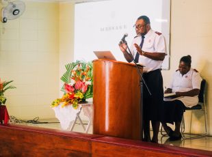 An officer sings and plays guitar in front of a congregation, accompanied by a girl also playing guitar.