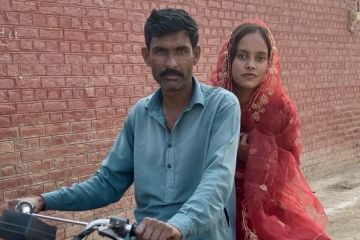 Nisha on the back of a motorcycle. A man is in front of her on the bike holding onto the handles.