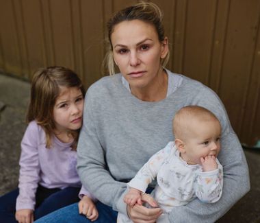 Mother looking distressed with a newborn in her arms, and a young girl by her side.
