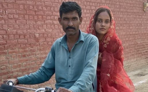 Nisha on the back of a motorcycle. A man is in front of her on the bike holding onto the handles.