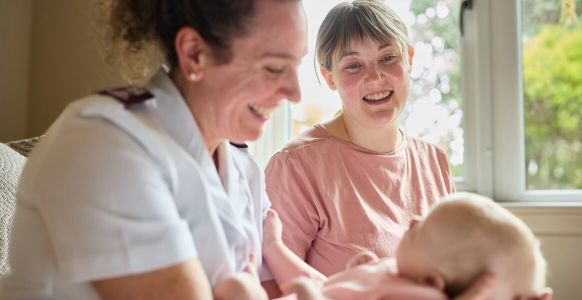 Emily smiling with Salvos personnel carrying her daughter