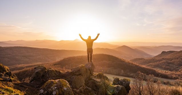 Man standing on hill with arms up facing sunset