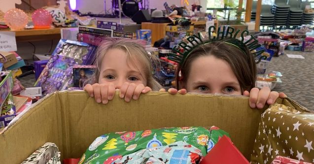 Two girls peek over box of donated gifts