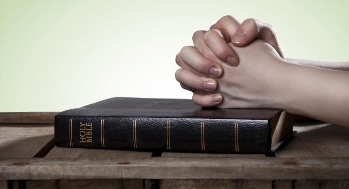 Praying hands resting on a Bible