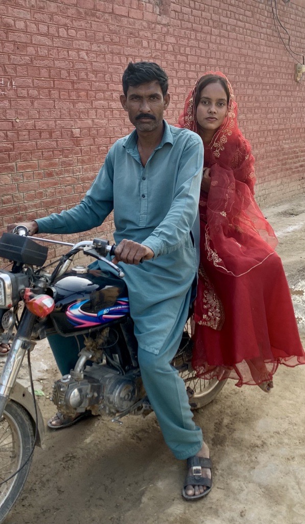 Nisha on the back of a motorcycle. A man is in front of her on the bike holding onto the handles.