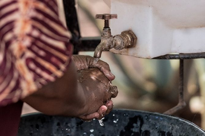 A close up view of hands being washed with water from an outdoor tank.