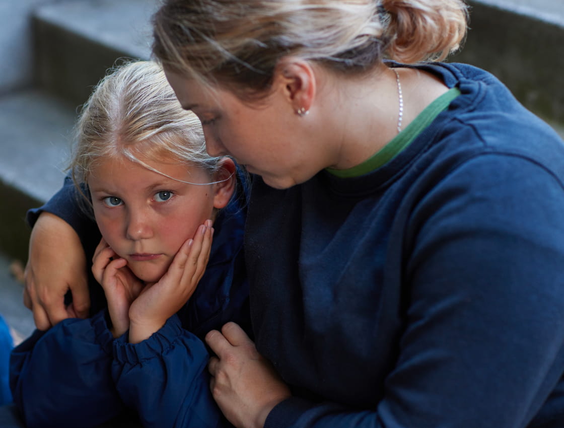 A primary school-aged girl appears stressed as her mother tries to comfort her.