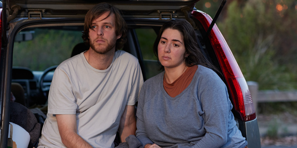 A young female and male looking distressed sitting in a car.