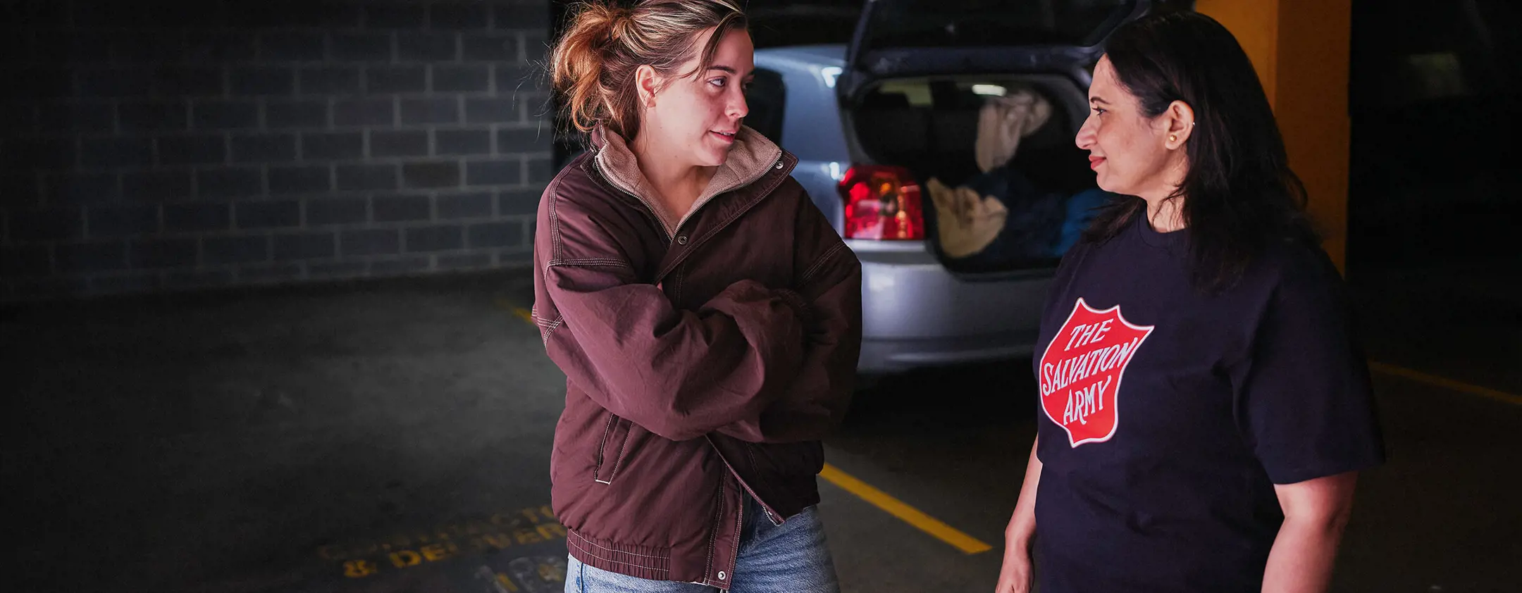 A young woman talks with a Salvos volunteer beside her car.