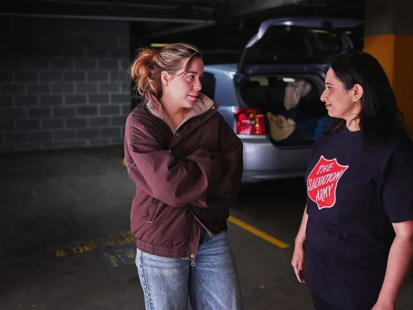 A young woman talks with a Salvos volunteer beside her car.