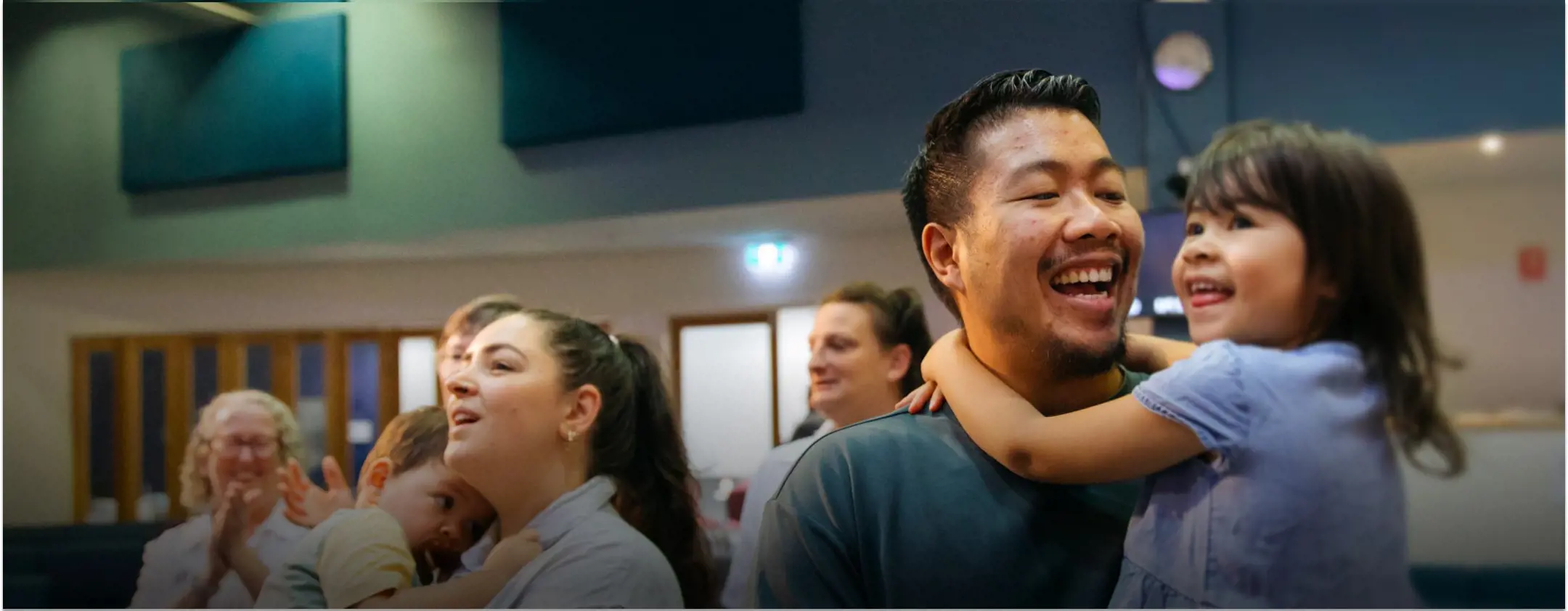 Two parents hold their young children as they all sing during a Sunday service.