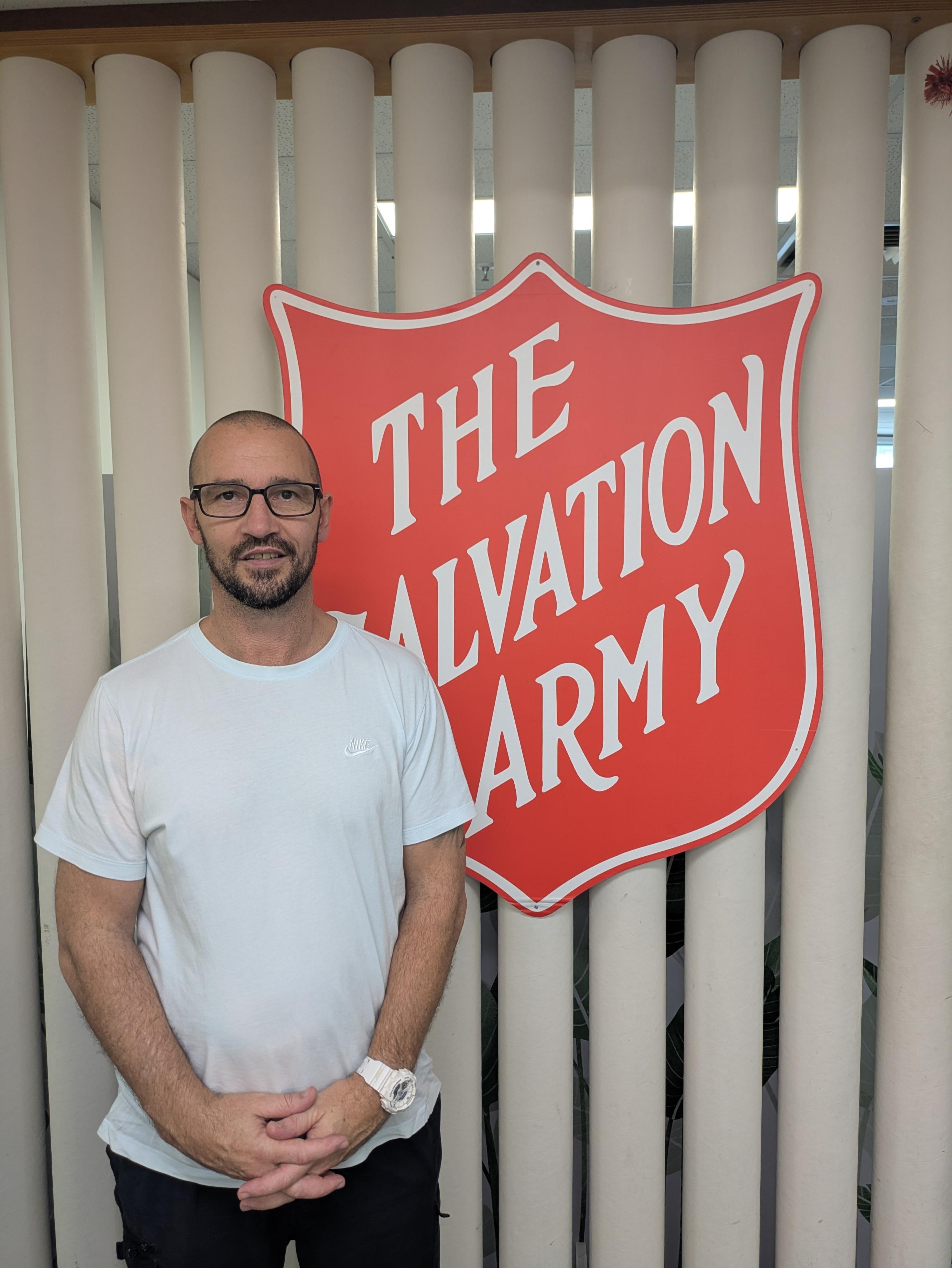Natham standing in front of The Salvation Army shield logo.