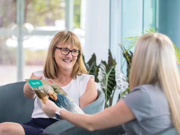 Two women sit together discussing a brochure that one is holding.