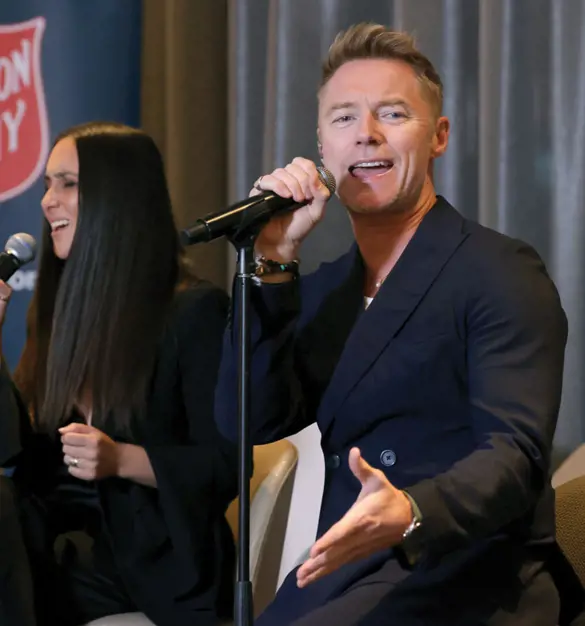 Ronan Keating is crooning with the help of another singer and a guitarist with a Salvos shield in the background.
