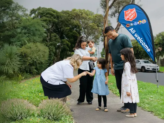 A Salvation Army officer warmly greeting a family of five on a path.