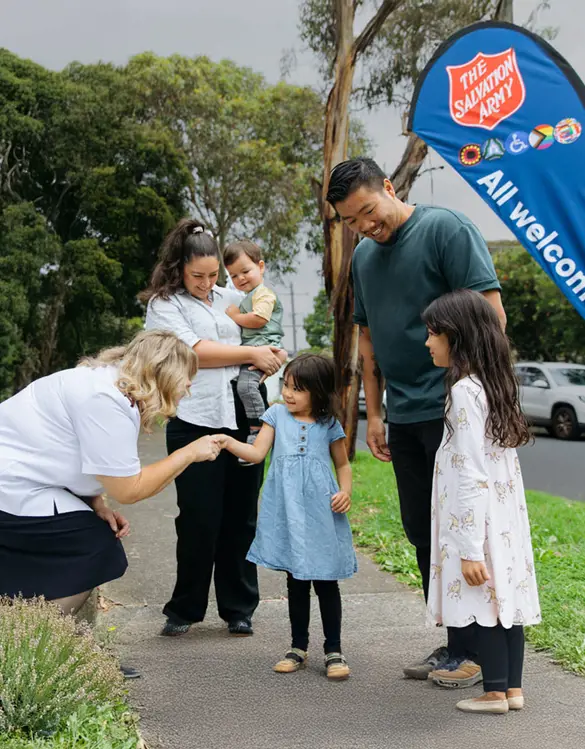 A Salvation Army officer warmly greeting a family of five on a path.