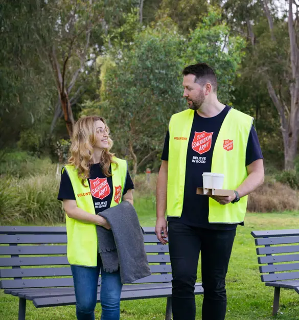 Two Salvation Army volunteers sharing a friendly conversation in a park, ready with warm coffee, blankets, and open hearts to support those doing it tough.