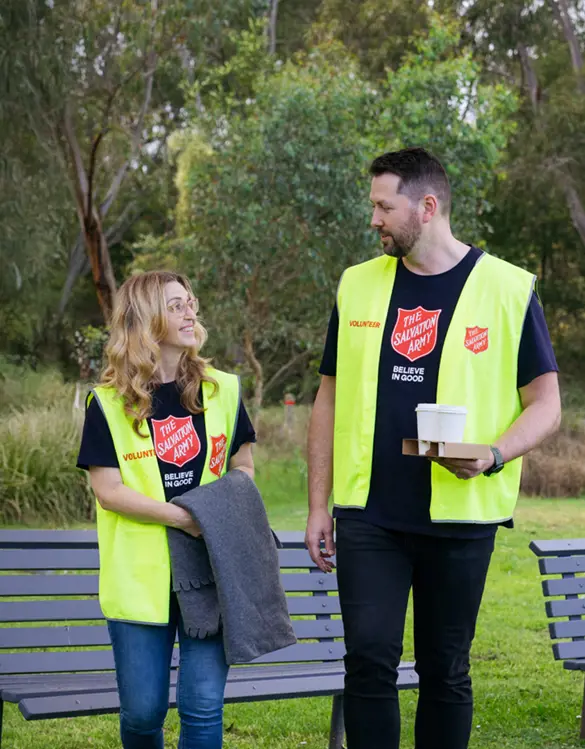 Two Salvation Army volunteers sharing a friendly conversation in a park, ready with warm coffee, blankets, and open hearts to support those doing it tough.