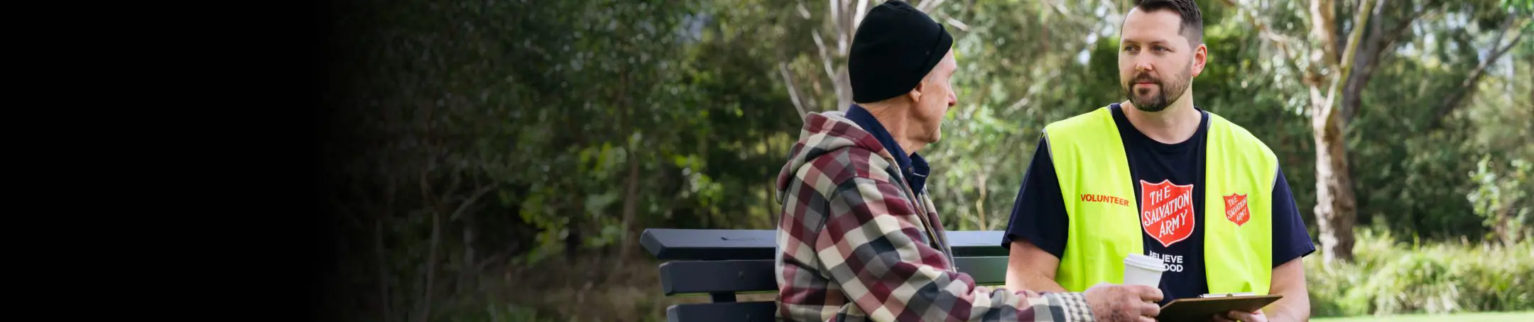 A Salvos volunteer and an older gentleman share a park bench, a coffee and chat.