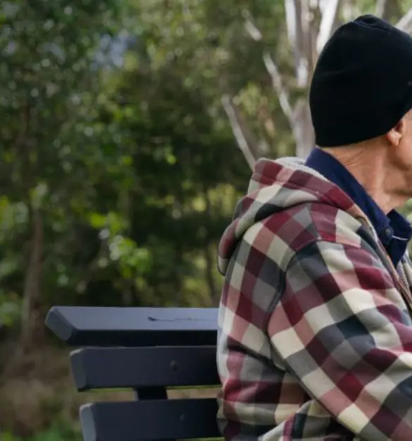 A Salvos volunteer and an older gentleman share a park bench, a coffee and chat.