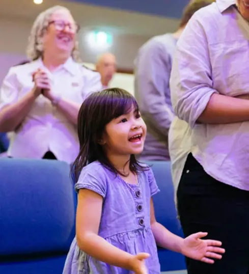 A young girl sings and claps enthusiastically during a church service with her family.