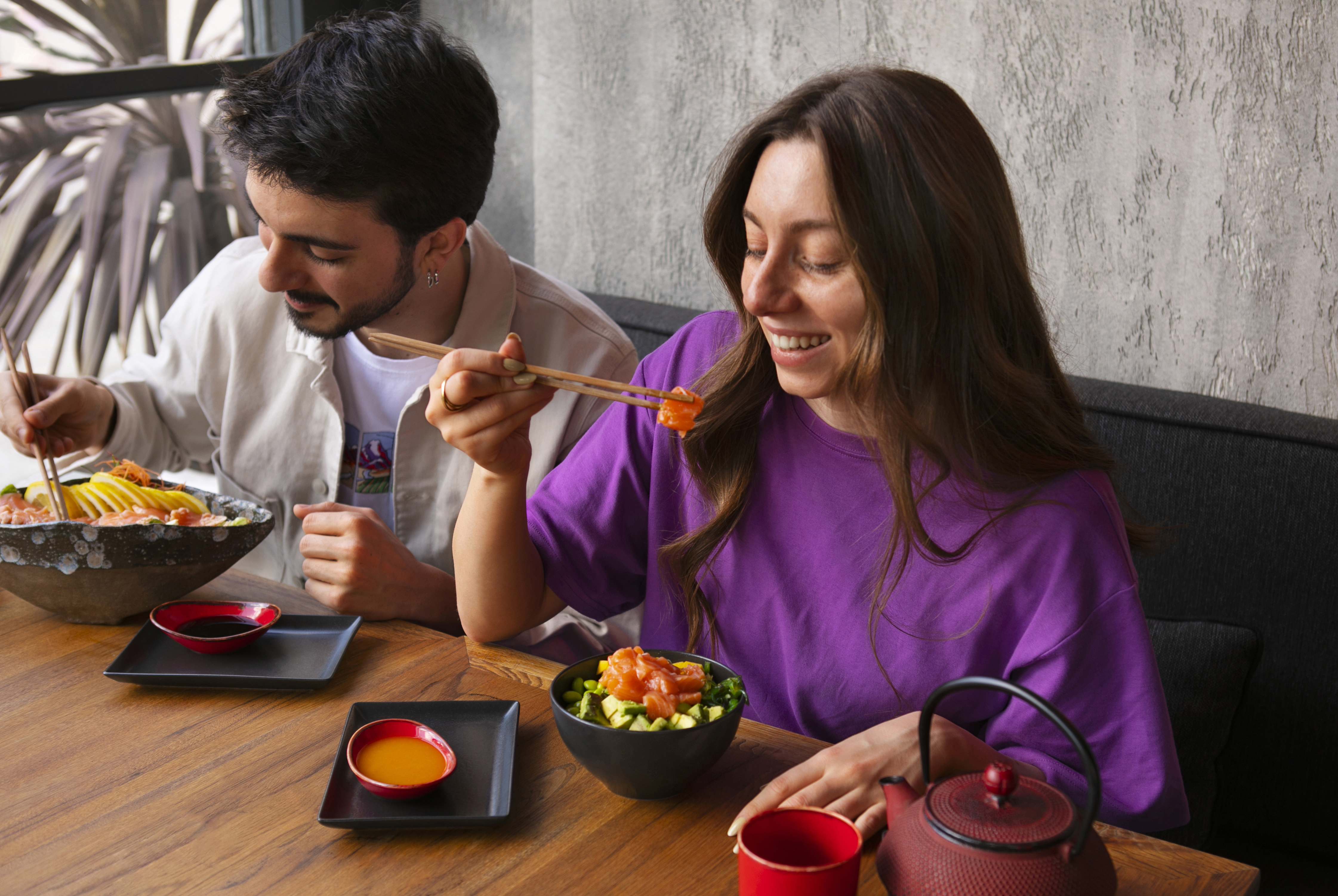 Two happy people eating salmon dishes with chopsticks at a restaurant table.