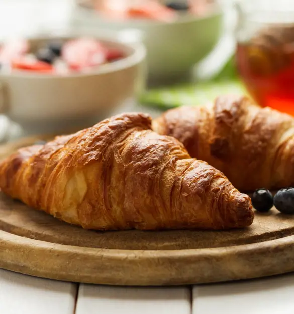Croissants on a wooden plate with some fresh blueberries.