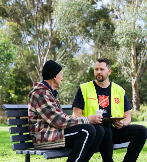 A Salvos volunteer listens to an older man tell his story on a park bench.
