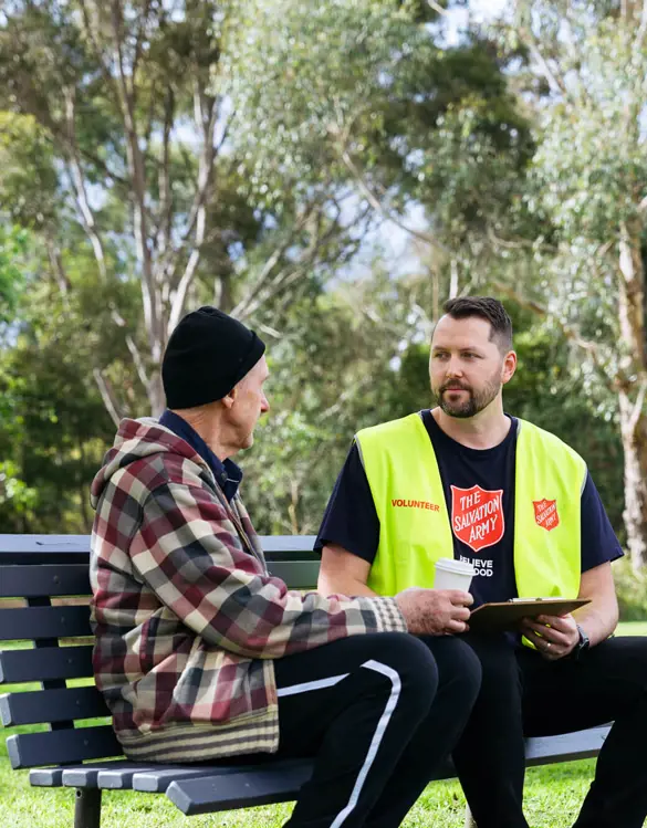 A Salvos volunteer listens to an older man tell his story on a park bench.