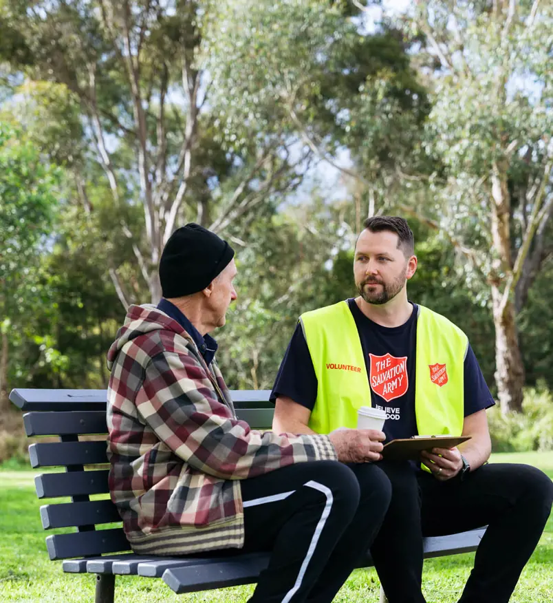 A Salvos volunteer listens to an older man tell his story on a park bench.