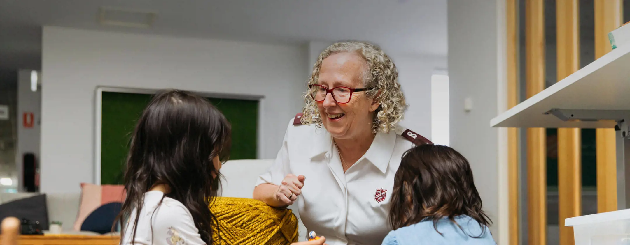 Two children playing with toys as female Salvos Officer is smiling.