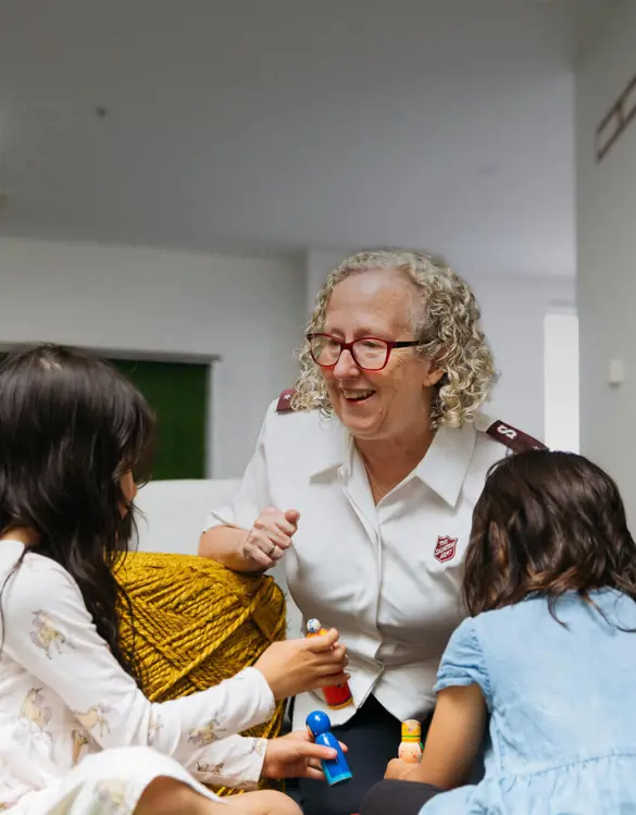 Two children playing with toys as female Salvos Officer is smiling.