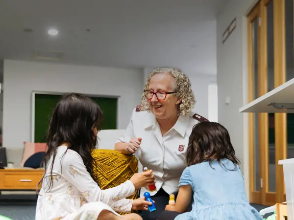 Two children playing with toys as female Salvos Officer is smiling.