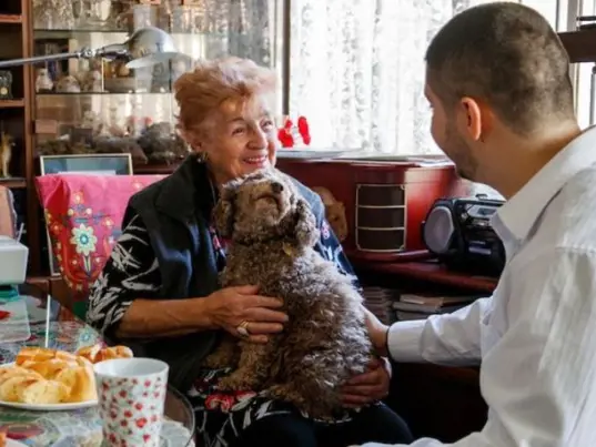 A older woman with a small dog on her lap talks with a Salvos volunteer