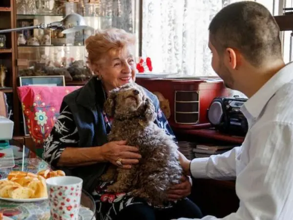 A older woman with a small dog on her lap talks with a Salvos volunteer