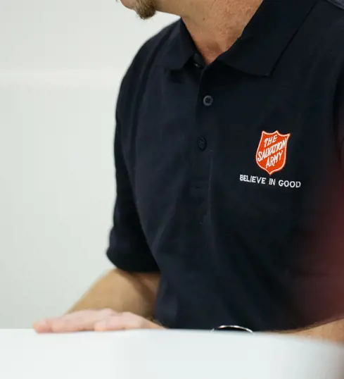 A smiling person wearing a Salvation Army polo shirt sitting at a welcome table.