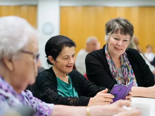 A diverse group of older community members enjoying fellowship and share photos on their phones..