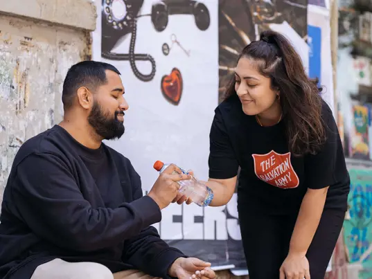 Salvation Army volunteer providing a man with bottled water.