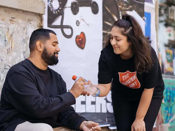 Salvation Army volunteer providing a man with bottled water.