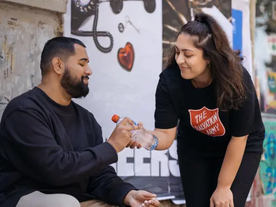 Salvation Army volunteer giving man bottled water.